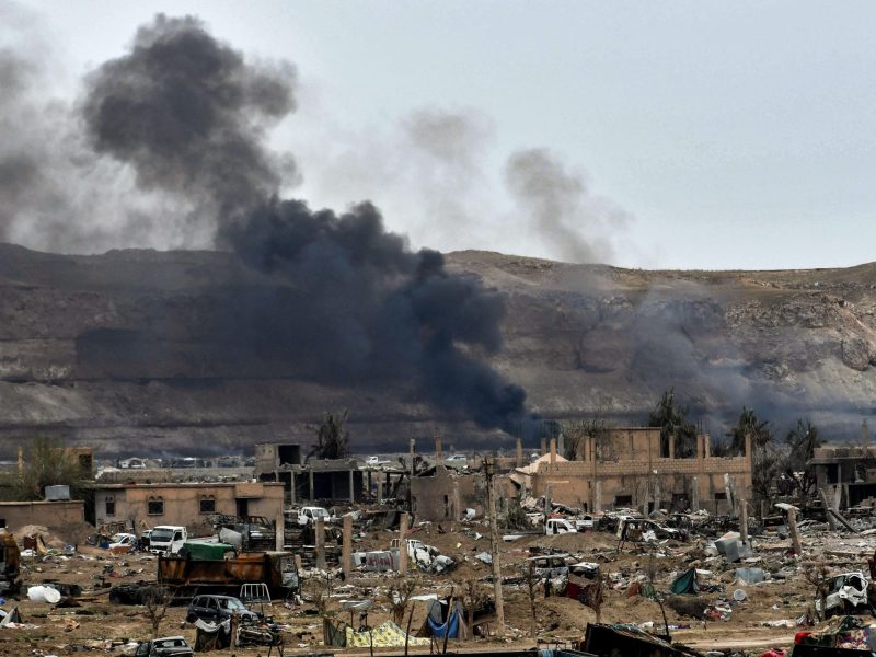 Photo of smoke rising behind destroyed vehicles and damaged buildings in the village of Baghouz in Syria's eastern Deir Ezzor province, taken March 24, 2019