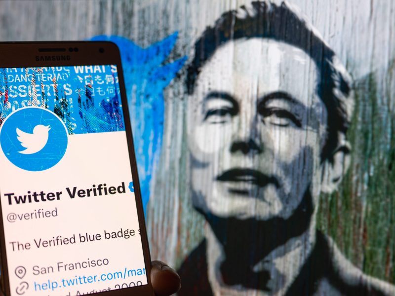 Twitter Verified icon seen on mobile screen with Elon Musk in the background illustration, in Brussels, Belgium, on December 11, 2022.