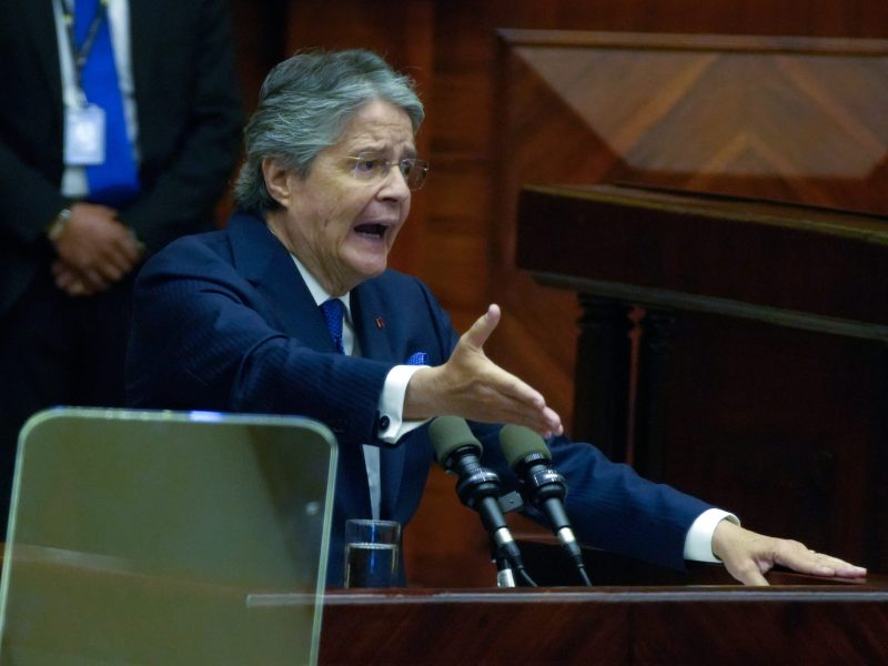 Guillermo Lasso stands at a podium in the National Assembly with one hand raised in an impassioned gesture and his mouth open, suggesting he is shouting.