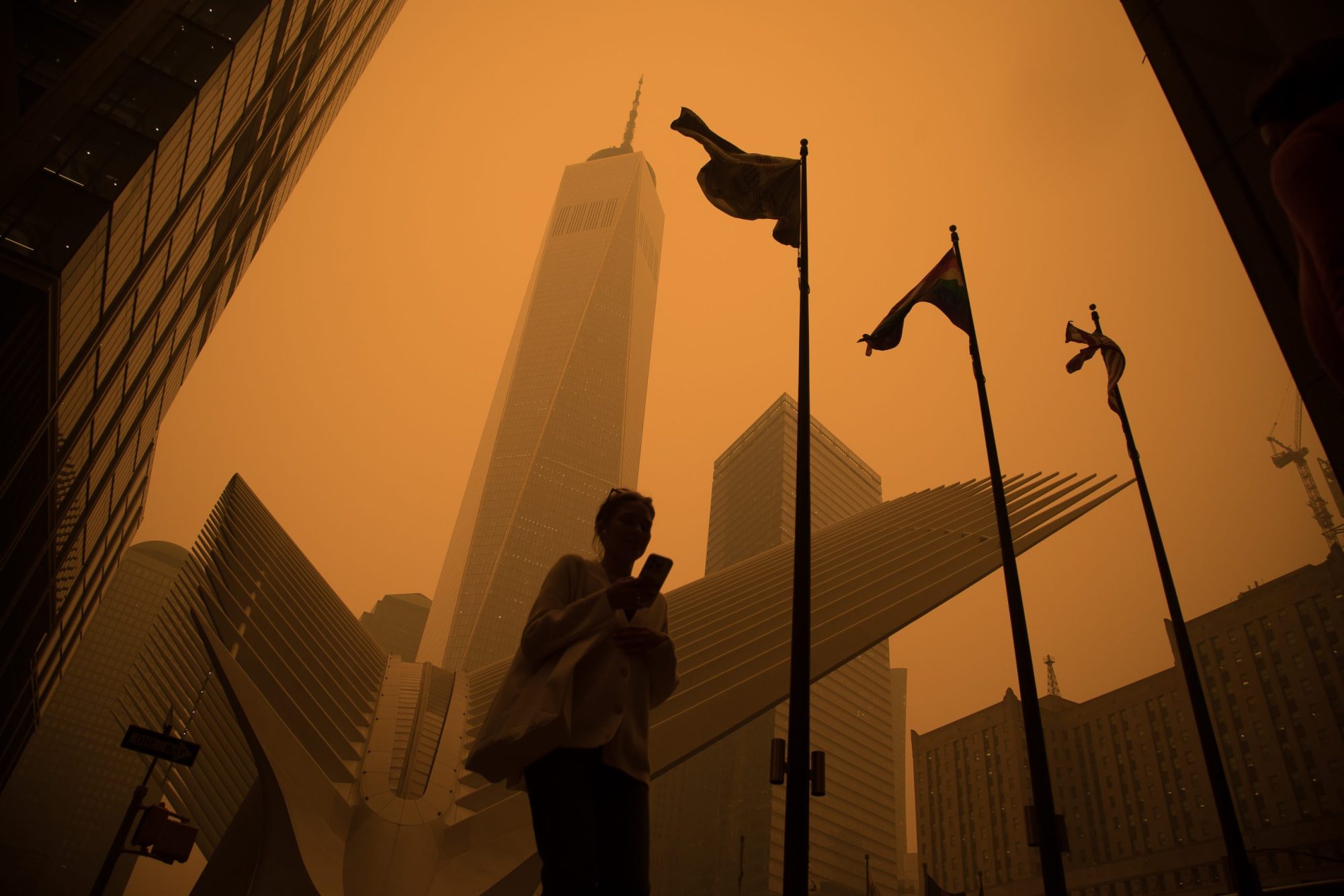 Low angle shot of a pedestrian walking in front of a skyscraper, the entire scene is shrouded in an eerie orange smog.