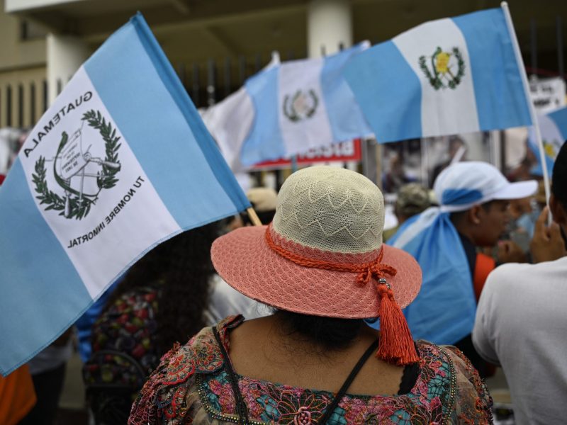 Rear shot of a woman in a brightly colored hat, carrying the Guatemalan flag