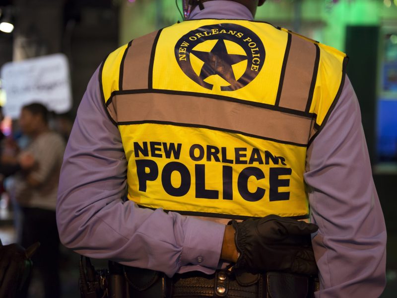 The back of a uniformed police officer wearing a vest that reads "New Orleans Police"